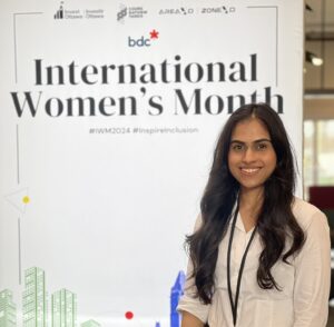 Female graduate smiling in front of Intl Women's Month poster