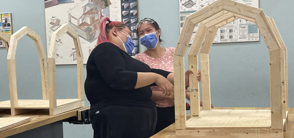 NYA participants Sky Kulluk (L) and Breana Mannilaq (R) share a laugh while learning to build a doghouse.