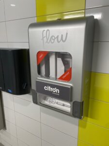 Photo of Aunt Flow dispensers in Algonquin College washroom. Dispenser is silver and has two small signs that read "free". 