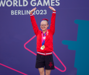 Kimana Mar holds up her hands in celebration at the Special Olympic World Summer Games in Berlin. Mar wears a red, Team Canada jacket, her medals and a smile. 