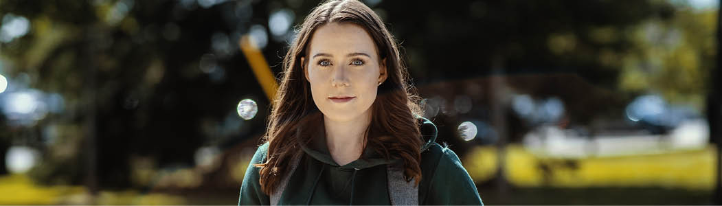 Student outside on a sunny day wearing an Algonquin College sweater and backback smiling at the camera. 