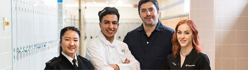 Four students in various different programs smiling at the camera in the hall. 