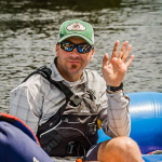 Jeff Jackson, in raft wearing hat and sunglasses waves to camera - Outdoor Adventure