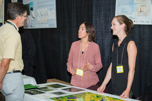 Two female applied research technicians speak with a male event attendee