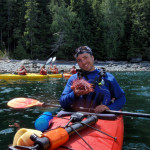 Damon outdoor adventure graduate in red kayak in river - Grad Success Stories