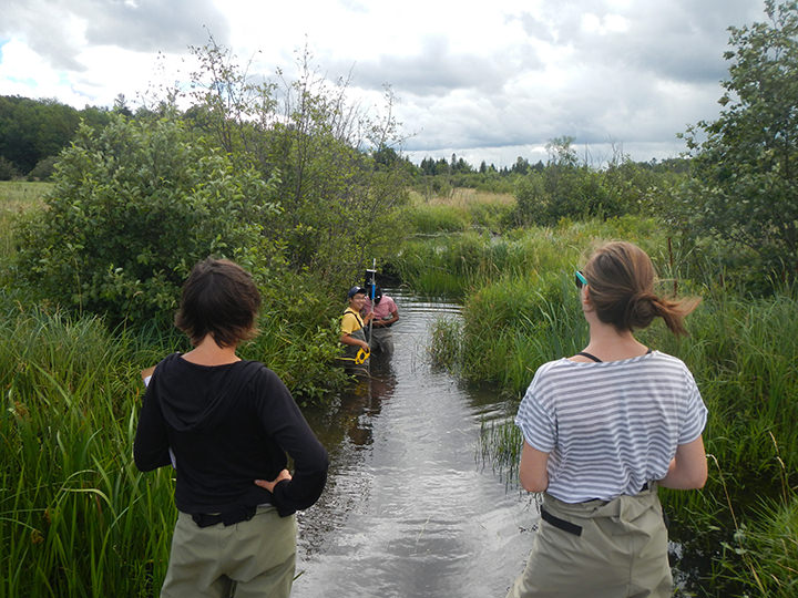 Two female students with their backs to the camera facing Buttermilk Creek, while two male students measure flow. 