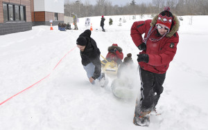 students pulling another student in a winter land kayak race for AC Hub winter carnival