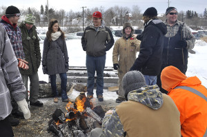 A group of students  around a fire pit - loggersports demo for AC Hub winter carnival