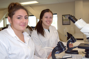 Two female students standing near a microscope