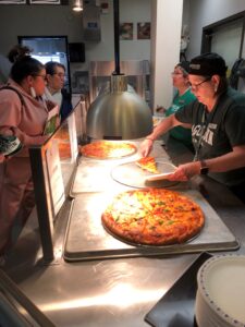Food Services staff serve homemade pizza to students and families.