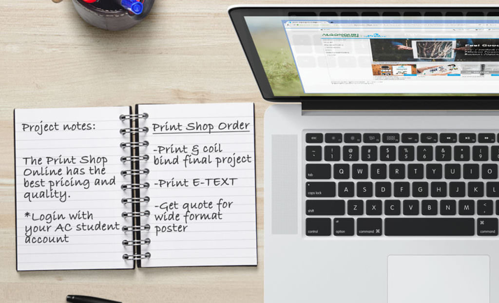 Image of a laptop displaying the Print Shop Online website with an open notebook beside it.