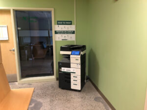 Image of a Konica Minolta black and white printer on the first floor of the Perth campus in the hallway outside of room 112.