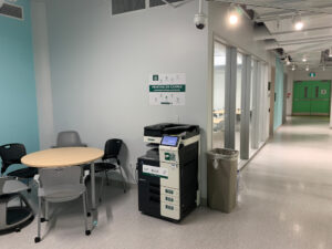 Image of one Konica Minolta black and white printer on the second floor of C building located in the hallway outside of room C264.
