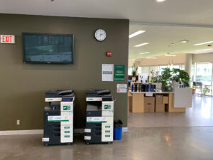 Image of two Konica Minolta colour printers on the second floor of E building located in the hallway outside of the AC Hub room E217.