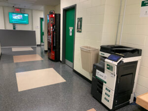 Image of a Konica Minolta black and white printer on the second floor of H building in the hallway outside of room H212.