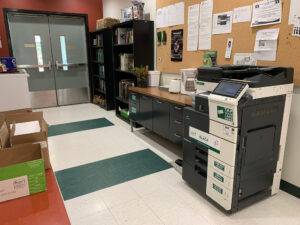 Image of a Konica Minolta black and white printer on the first floor of M building in the hallway outside of room M108.