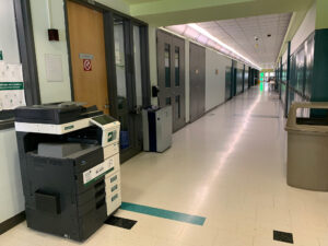 Image of a Konica Minolta black and white printer on the first floor of N building in the hallway outside of room N101.