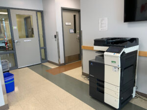 Image of a Konica Minolta black and white printer on the first floor of V building in the main lobby outside of room V105.